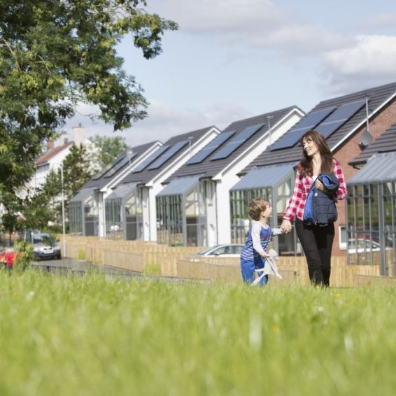 A woman and a little boy walk through the grass next to a housing development