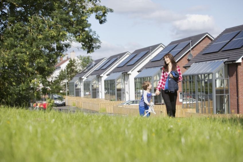 A woman and a little boy walk through the grass next to a housing development 